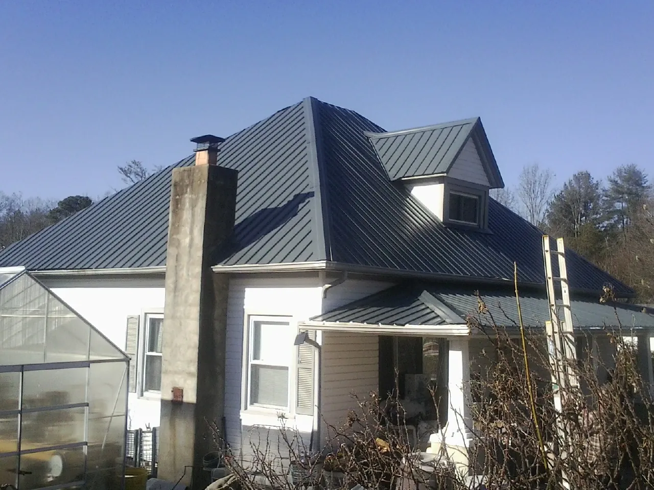 Dark blue standing seam metal roof on a white farmhouse with dormer — Slate & Tile Roof Repair by Roofing Brothers in Crapo