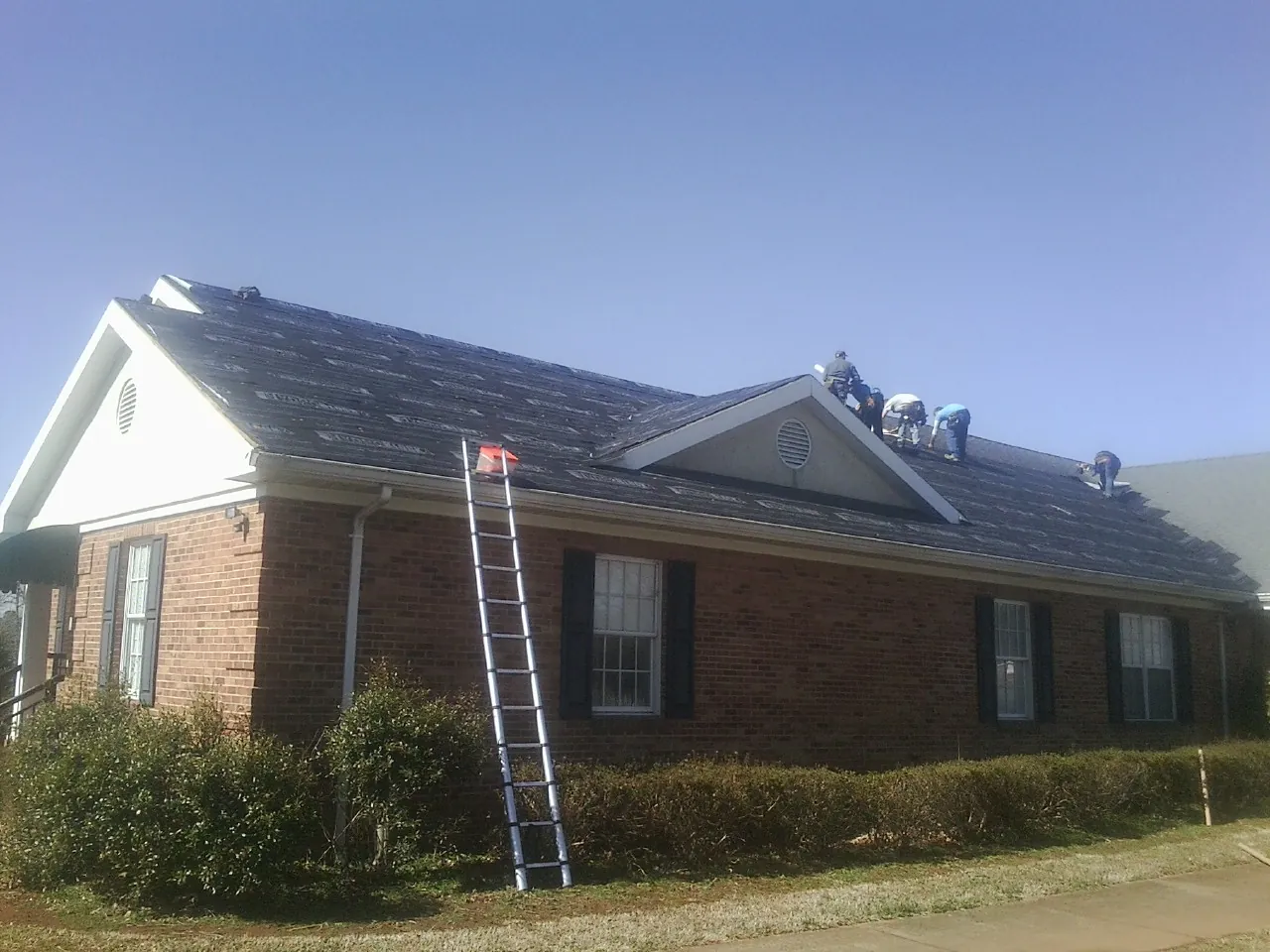 Crew tearing shingles off a brick ranch roof with a ladder set — Emergency Roof Repair work by our crew in Crapo