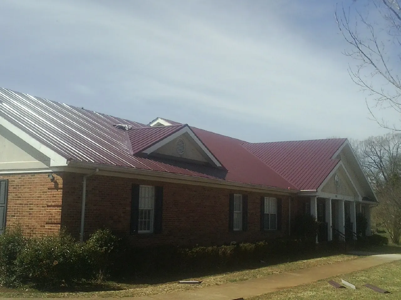 Red metal roof with gabled entries on a long brick building, from a Hail Damage Roof Repair job in Crapo