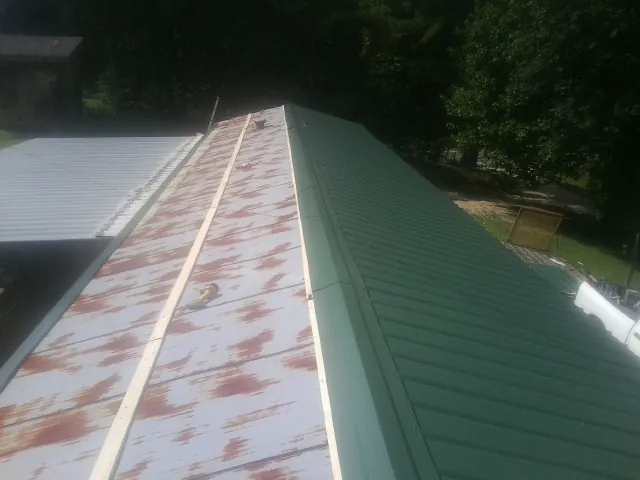 Old rusted panels beside newly installed green metal roofing — Wind Damage Roof Repair by Roofing Brothers in Crapo