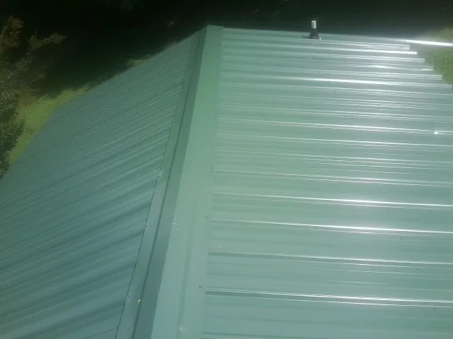 New green metal panels meeting at the ridge of a roof — Flat Roof Repair work by our crew in Crapo
