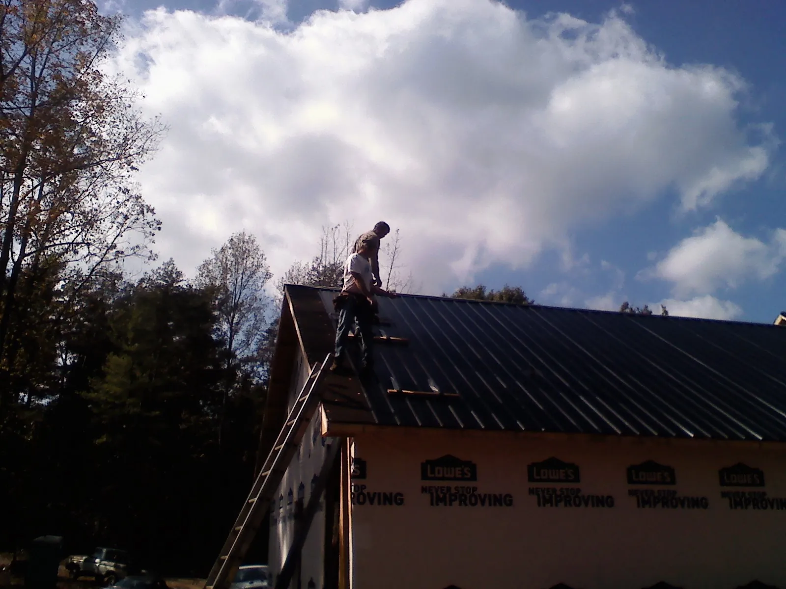 Roofer fastening dark metal panels high against a cloudy sky, from a Roof Inspection job in Crapo