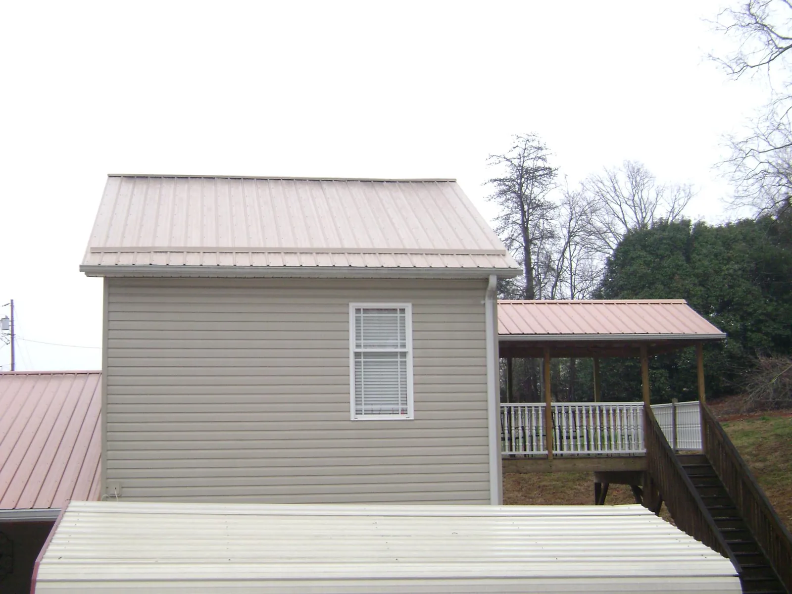 Tan metal roofs on a two story addition and attached porch, from a Roof Replacement job in Crapo